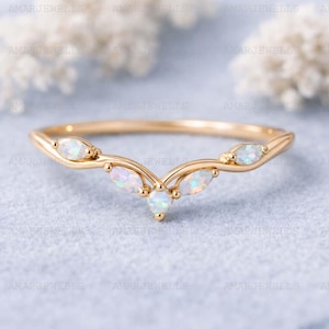 May include: A gold ring with a curved design, set with opal gemstones. The opals are pear and marquise-shaped, displaying an iridescent sheen. The ring's band is slender and elegant, with a delicate appearance.