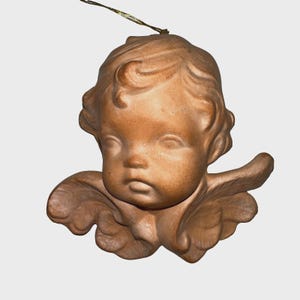 May include: A terracotta-colored cherub ornament with detailed facial features, curly hair, and small wings. The cherub has a serious expression and is suspended by a gold-colored string, suitable for hanging as a decoration.