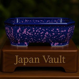 Könnte beinhalten: Blauer Keramik-Bonsai-Topf mit rosa Sprenkeln. Der rechteckige Topf hat eine achteckige Form und steht auf einem Holzsockel mit dem goldenen Schriftzug "Japan Vault".