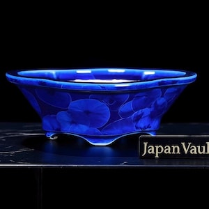 Könnte beinhalten: Eine leuchtend blaue Keramikschale mit floralem Muster. Die Schale hat eine breite, flache Form und steht auf drei kleinen Füßen. Der Text "Japan Vault" wird auf einem schwarzen rechteckigen Schild angezeigt.