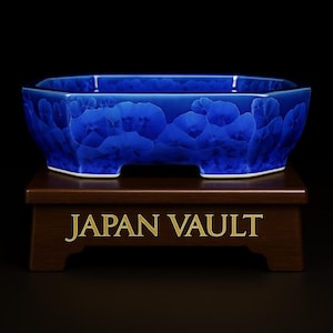 May include: A striking blue ceramic bonsai pot with a distinctive floral design. The pot is displayed on a dark wooden stand, featuring the gold text "JAPAN VAULT". The pot has a rectangular shape with softened edges.