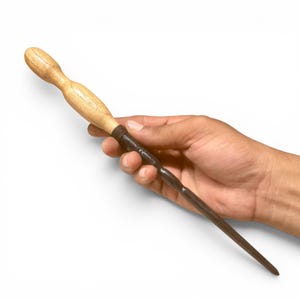 May include: A handheld wand featuring a light-coloured, smooth wooden handle with a rounded grip and a dark, textured, tapered shaft. The two sections are joined by a dark, ribbed band, creating a distinct contrast between the light and dark elements.