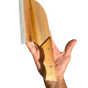 May include: A wooden cleaver with a light brown handle and a silver blade. The handle is attached to the blade with two silver rivets. The cleaver is held against a white background.