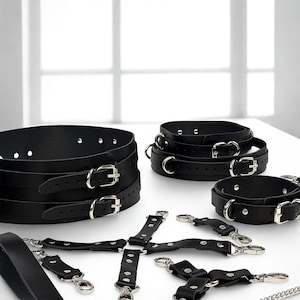 May include: Black leather restraints with silver-colored buckles and hardware. The image shows a variety of items, including collars, cuffs, and straps, all designed with a focus on functionality and a sleek aesthetic. The products are arranged on a white surface.