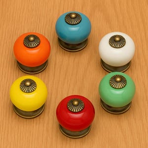May include: A set of six brightly coloured ceramic cabinet knobs. The knobs are arranged in a circle and feature shades of orange, blue, white, green, yellow, and red. Each has a bronze-toned base and decorative centre.