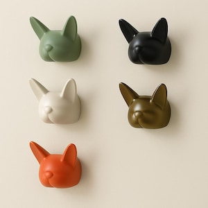 Puede incluir: Cinco perchas de pared decorativas con forma de cabeza de bulldog francés. Los ganchos son de varios colores: verde, negro, blanco, verde oliva y naranja. Cada gancho tiene un acabado liso y mate.