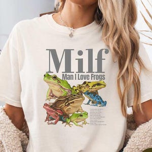 A woman wearing a white t-shirt with a graphic of frogs and the text "Milf Man I Love Frogs" printed on it.