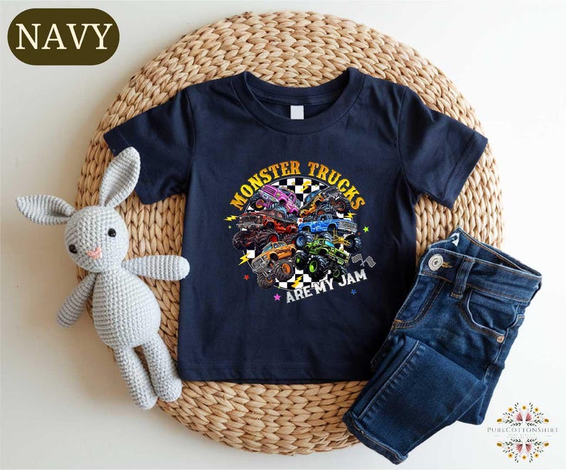 A navy blue t-shirt with a graphic of monster trucks and the text "MONSTER TRUCKS ARE MY JAM" printed on it, along with a pair of blue jeans and a crocheted stuffed rabbit.