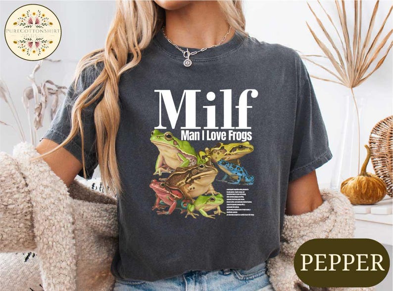 A woman wearing a gray t-shirt with a graphic design of various colored frogs.