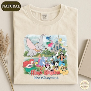 A t-shirt with a colorful graphic design depicting various Disney characters from the Magic Kingdom, including Dumbo, Minnie Mouse, Mickey Mouse, Donald Duck, and Goofy, along with a castle and a lake.