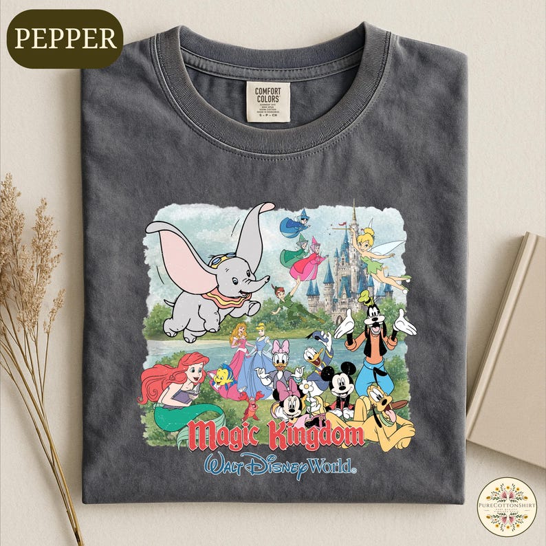 A gray t-shirt with a colorful graphic design depicting various Disney characters from the Magic Kingdom, including an elephant, mermaid, and other iconic figures.