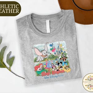 A gray t-shirt with a Disney-themed graphic design, including characters from the Disney animated films, is displayed on a white surface.