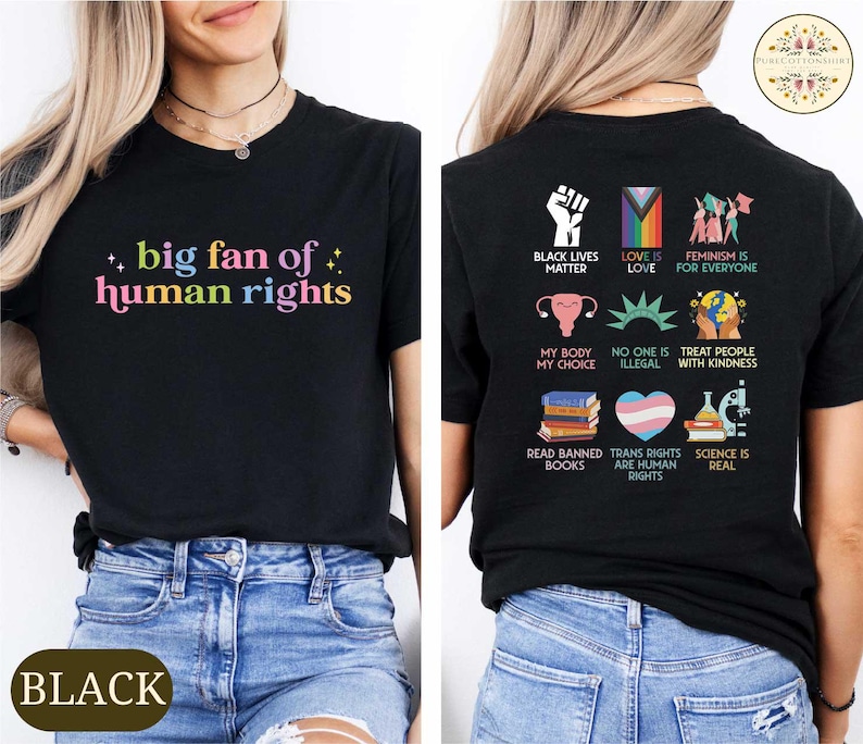 May include: Black t-shirt with the text "big fan of human rights" in colorful letters. The back of the shirt features various social justice slogans and symbols, including "Black Lives Matter" and "Trans Rights Are Human Rights".