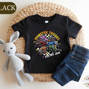 a black t-shirt with a colorful graphic design of monster trucks, along with a stuffed rabbit and a pair of blue jeans.