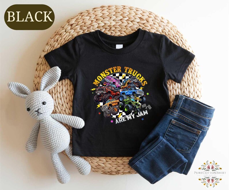 a black t-shirt with a colorful graphic design of monster trucks, along with a stuffed rabbit and a pair of blue jeans.