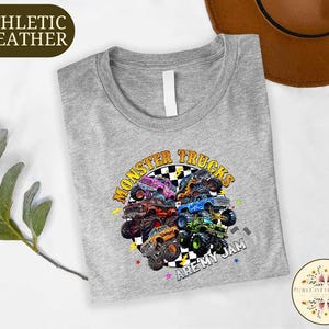 a gray t-shirt with a colorful graphic design of monster trucks, along with the text "MONSTER TRUCKS ARE MY TEAM" printed on it.