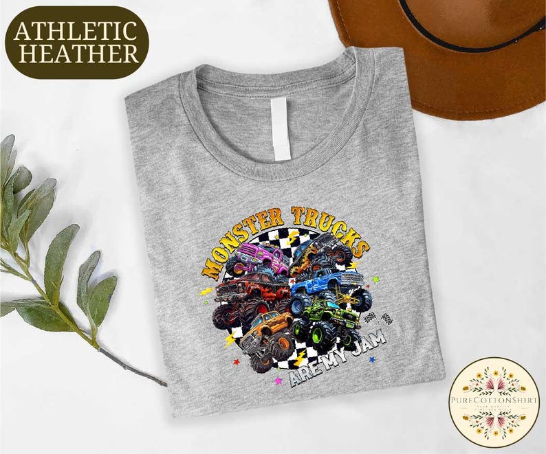 a gray t-shirt with a colorful graphic design of monster trucks, along with the text "MONSTER TRUCKS ARE MY TEAM" printed on it.