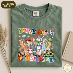 A green t-shirt with a colorful graphic design featuring characters from the Toy Story franchise, including Woody, Buzz Lightyear, and other beloved characters.