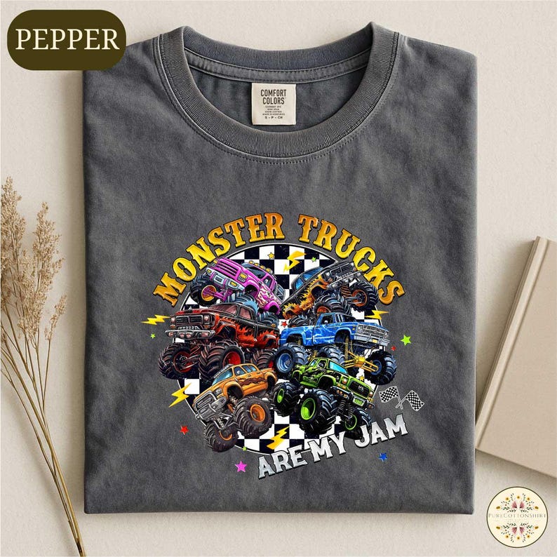 A gray t-shirt with a graphic design featuring various monster trucks and the text "MONSTER TRUCKS ARE MY JAM" printed on it.