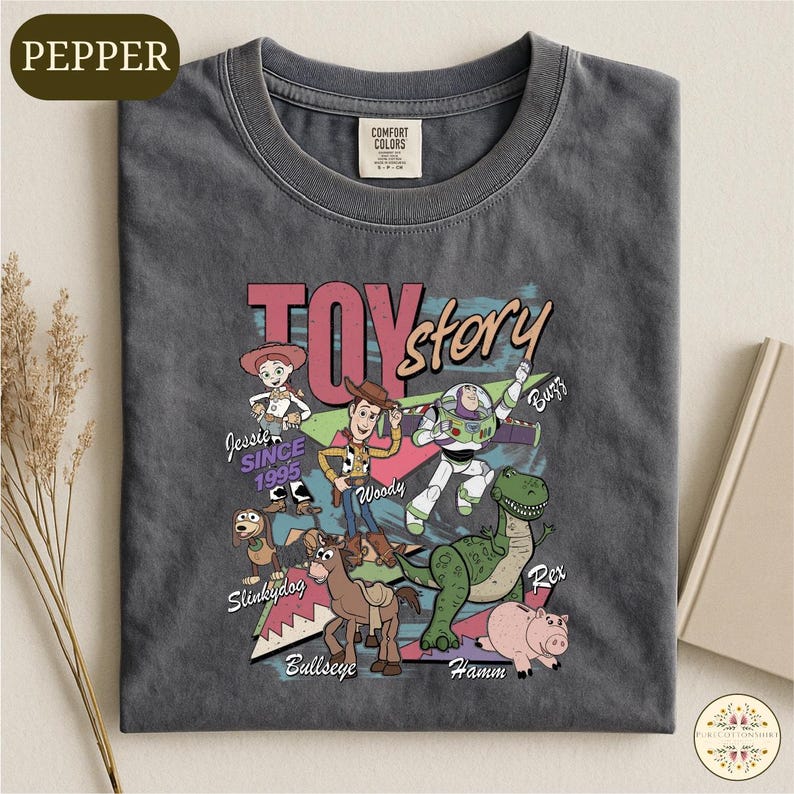 A gray t-shirt with a colorful graphic design featuring characters from the Toy Story movie, including Woody, Buzz Lightyear, Slinky, and Hammy.