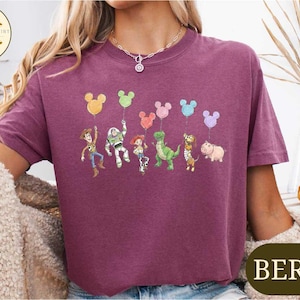 A person wearing a purple t-shirt with a graphic of characters from the Toy Story franchise, including Woody, Buzz Lightyear, and other beloved characters.