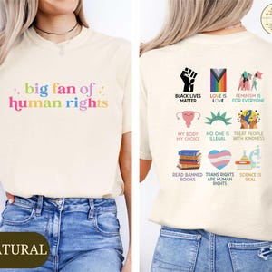 May include: Cream-colored t-shirt with the text "big fan of human rights" in rainbow colors. The back of the shirt features various graphics and phrases, including "Black Lives Matter" and "Love is Love."