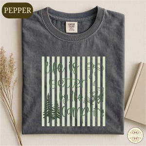 A gray t-shirt with a graphic design featuring a green and white striped pattern, along with the text "Life is better at the Campfire" printed on it.