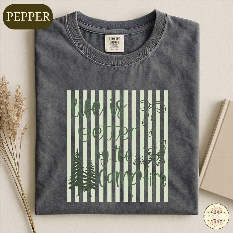 A gray t-shirt with a graphic design featuring a green and white striped pattern, along with the text "Life is better at the Campfire" printed on it.