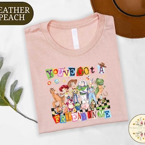 A pink t-shirt with a colorful graphic design featuring characters from the Toy Story franchise, along with the text "You've got a friend in me".