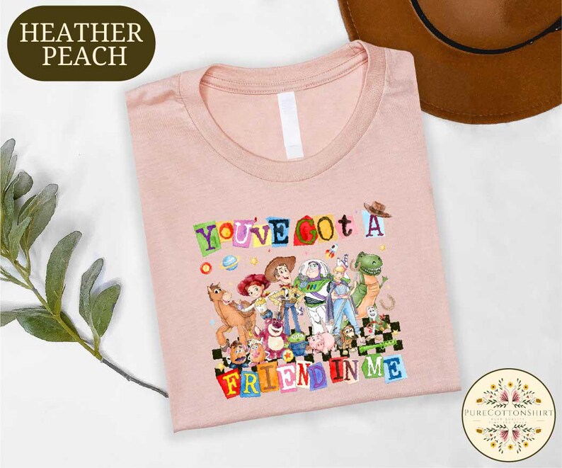 A pink t-shirt with a colorful graphic design featuring characters from the Toy Story franchise, along with the text "You've got a friend in me".