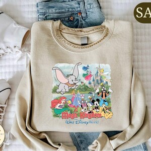 A beige sweatshirt with a Disney-themed graphic, including characters like Dumbo, Mickey Mouse, and other iconic Disney characters, along with the text "Magic Kingdom" and "Walt Disney World".