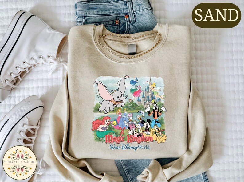 A beige sweatshirt with a Disney-themed graphic, including characters like Dumbo, Mickey Mouse, and other iconic Disney characters, along with the text "Magic Kingdom" and "Walt Disney World".