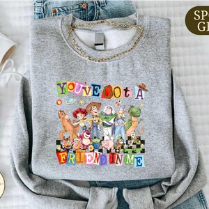 A gray sweatshirt with a colorful graphic design featuring characters from the Toy Story movie, along with the text "You've Got a Friend in Me".
