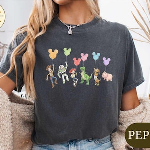 A woman wearing a black t-shirt with a graphic of characters from the Toy Story movie, including Woody, Buzz Lightyear, and other beloved characters, along with colorful balloons.