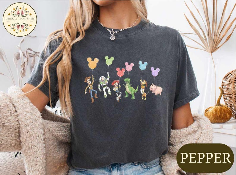 A woman wearing a black t-shirt with a graphic of characters from the Toy Story movie, including Woody, Buzz Lightyear, and other beloved characters, along with colorful balloons.