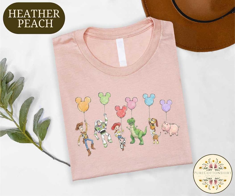 A pink t-shirt with a cartoon character design featuring a group of five Disney characters holding balloons, including a dinosaur, a pig, a piggy, a boy, and a girl.