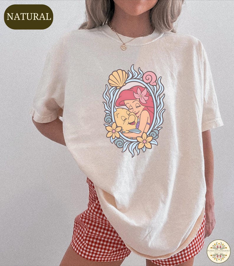 A person wearing a white t-shirt with a graphic of a mermaid and a flower design.
