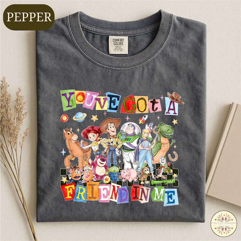 A gray t-shirt with a colorful graphic design featuring characters from the Toy Story movie, including Woody, Buzz Lightyear, and other beloved characters.