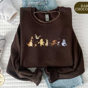 a brown sweatshirt with a line of cartoon animal characters printed on it, along with a pair of jeans and sneakers.