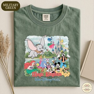 A green t-shirt with a printed design featuring various Disney characters from the Magic Kingdom, including Dumbo, Minnie Mouse, Mickey Mouse, Donald Duck, and other iconic figures.