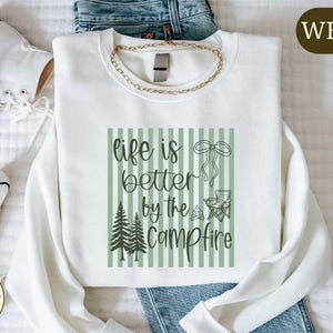 a white t-shirt with a graphic design, a pair of jeans, and a pair of white sneakers, all laid out on a bed.