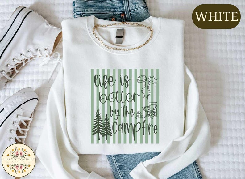 a white t-shirt with a graphic design, a pair of jeans, and a pair of white sneakers, all laid out on a bed.