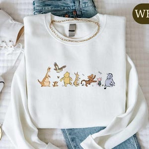 A white t-shirt with a graphic of Winnie the Pooh and his friends, along with a pair of jeans and white sneakers.