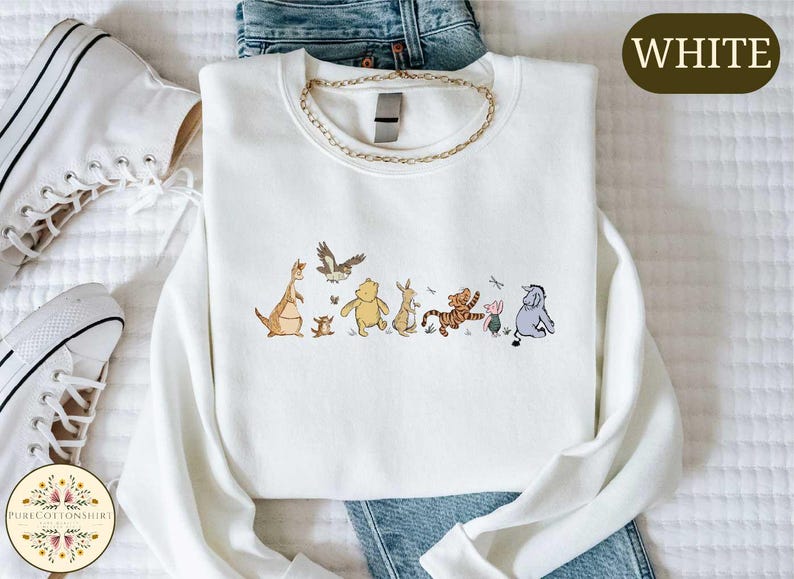 A white t-shirt with a graphic of Winnie the Pooh and his friends, along with a pair of jeans and white sneakers.