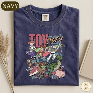 A navy blue t-shirt with a colorful graphic design featuring characters from the Toy Story movie, including Woody, Buzz Lightyear, and other beloved characters.