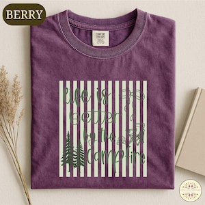 a purple t-shirt with a graphic design on it, which includes a quote and some forest-related elements.