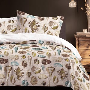 May include: A beige duvet cover and pillow set featuring a seashell design in brown, green, and blue. The bedding is on a bed with white sheets and pillows. The room has a dark wall and a wooden bedside table.