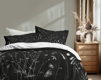 Könnte beinhalten: Schwarz-weißes Blumenbettwäsche-Set. Das Set beinhaltet einen Bettbezug und Kissenbezüge mit einem botanischen Design. Der Bettbezug und die Kissenbezüge haben einen schwarzen Hintergrund mit weißen Blumen- und Pflanzenillustrationen. Die Bettwäsche befindet sich auf einem Bett in einem Schlafzimmer.