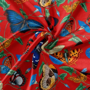 May include: Red fabric with a repeating pattern of colorful butterflies. The butterflies are in various poses and have different wing patterns. The fabric has a silky texture.