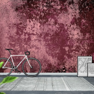 Könnte beinhalten: Ein weißes Fahrrad mit schwarzen Reifen und einem schwarzen Sattel steht vor einer roten und pinkfarbenen strukturierten Wand. Zwei schwarze gerahmte Karten liegen rechts neben dem Fahrrad auf dem Boden. Die Karte links zeigt New York City und die Karte rechts zeigt Paris.